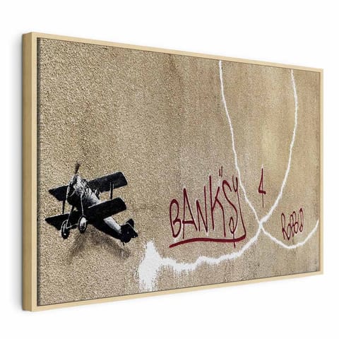 ⁨Obraz - Samolot Banksy (1-częściowy) - graffiti czerwone napisy na tle muralu (rozmiar 60x40, wykończenie W ramie drewnianej naturalnej)⁩ w sklepie Wasserman.eu