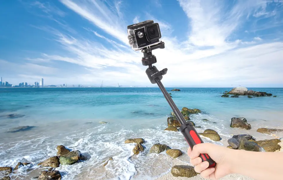 dłoń trzymająca selfie stick PULUZ ze sportową kamerą na tle morza