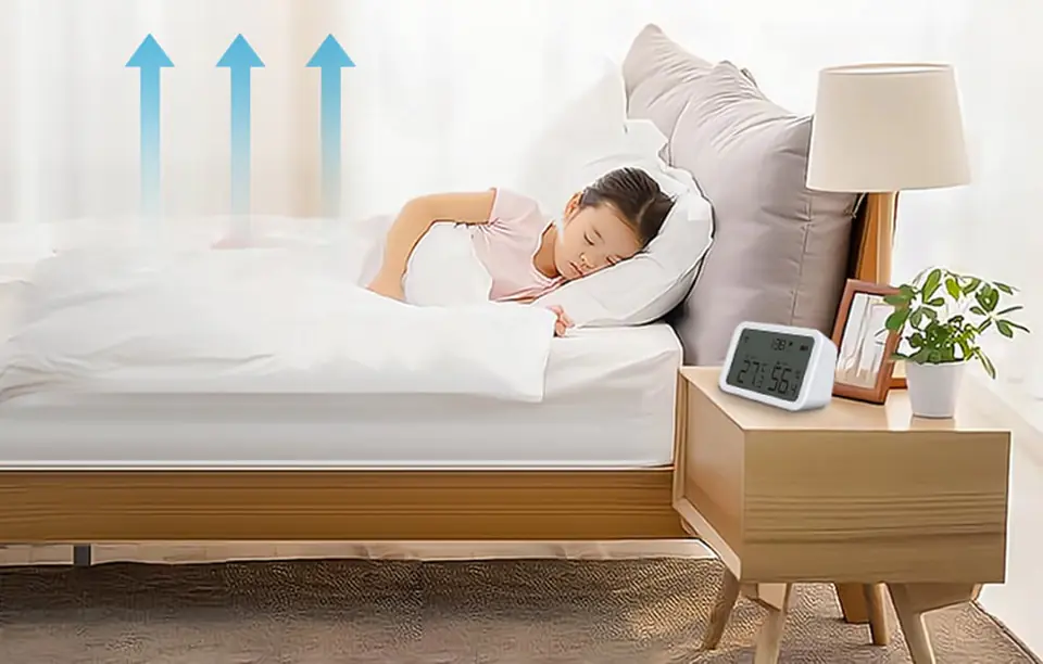 Czujnik temperatury i wilgotności NEO NAS-TH02W z wyświetlaczem Zigbee TUYA postawiony na szafce nocnej przy łóżku, w którym śpi dziecko.