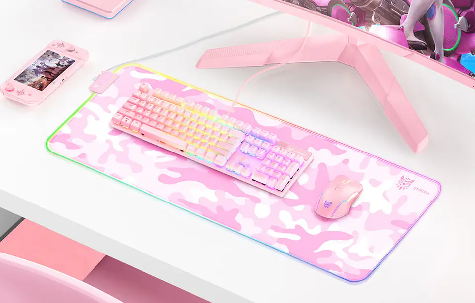 Białe biurko, na którym widoczna jest różowa podkładka gamingowa Onikuma MP005. Na podkładce umieszczono różową klawiaturę i myszkę. Z lewej strony widać różowe Nintendo Switch.