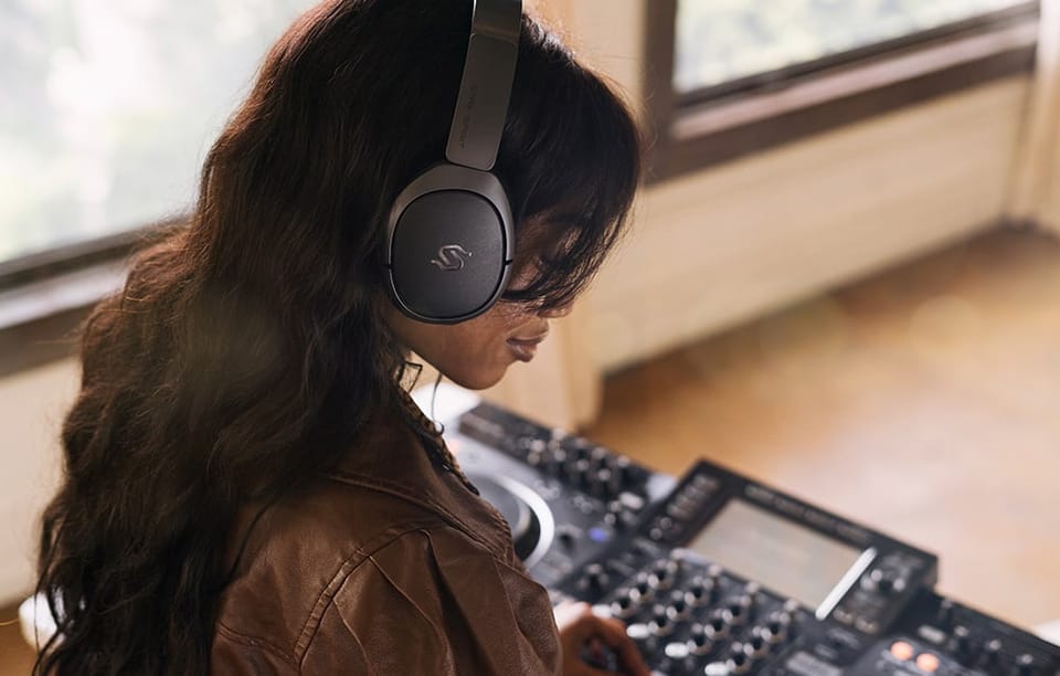 kobieta z czarnymi słuchawkami na głowie siedząca nad mikserem dźwięku