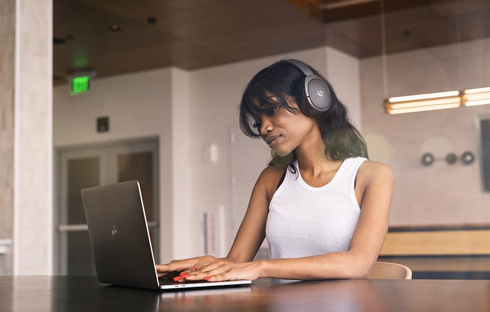 kobieta pracująca na laptopie, na głowie ma czarne słuchawki nauszne