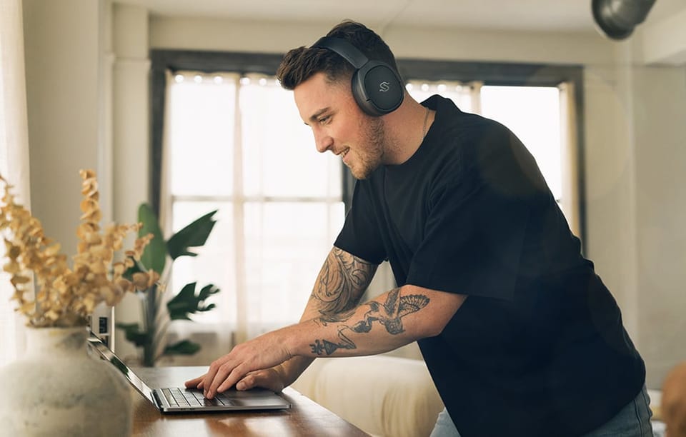 mężczyzna z czarnymi słuchawkami nausznymi na głowie korzystający z laptopa w jasnym salonie