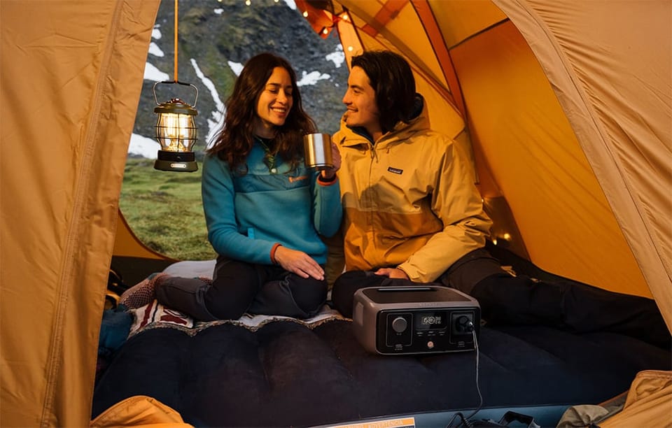 Para uśmiechniętych osób siedzi w namiocie na dmuchanym materacu z podłączoną stacją EcoFlow RIVER 3