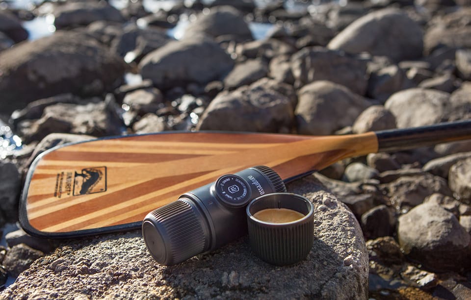 Przenośny ekspres do kawy z kubkiem kawy leży na kamieniu obok pomarańczowo-czarnego wiosła.