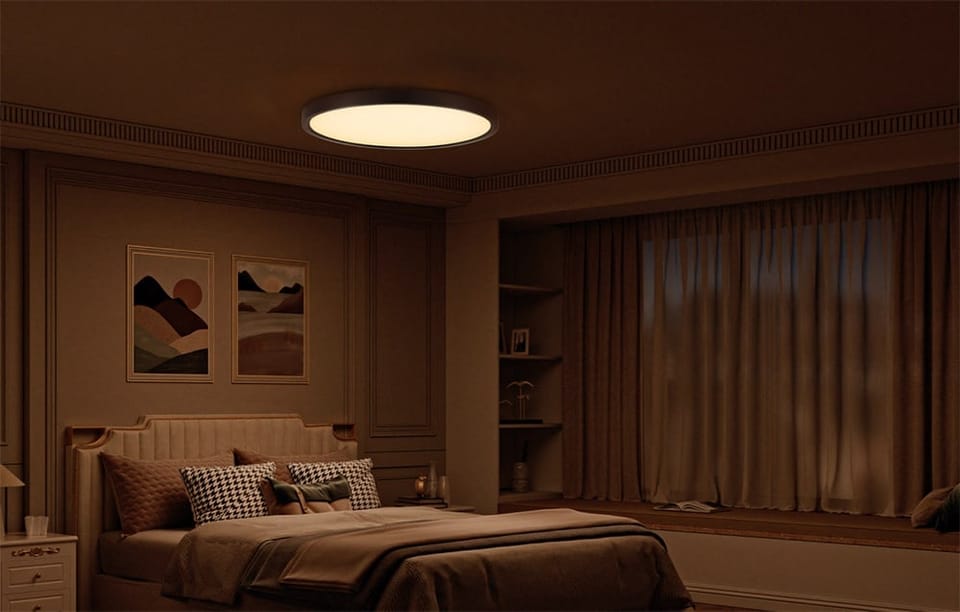 Lampa sufitowa Yeelight Meteor C500 świecąca w przyciemnionej sypialni z beżową pościelą i obrazami nad łóżkiem.