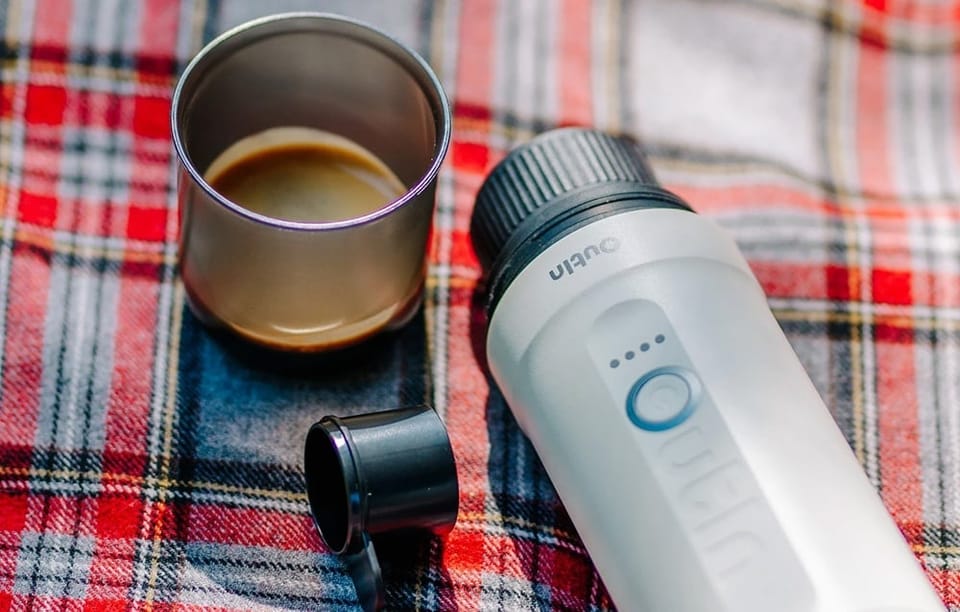 Bezprzewodowy ekspres do kawy Outin, kubek i miarka leżą na czerwonym kocu w kratkę.