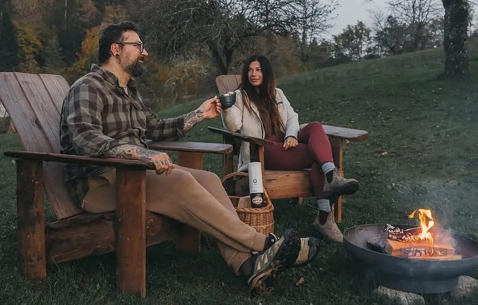 Mężczyzna i kobieta siedzą na krzesłach i piją kawę. Przed nimi pali się ognisko.