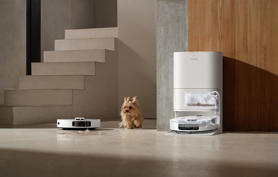 Robot sprzątający odkurza podłogę obok małego psa i stacji dokującej przy schodach.