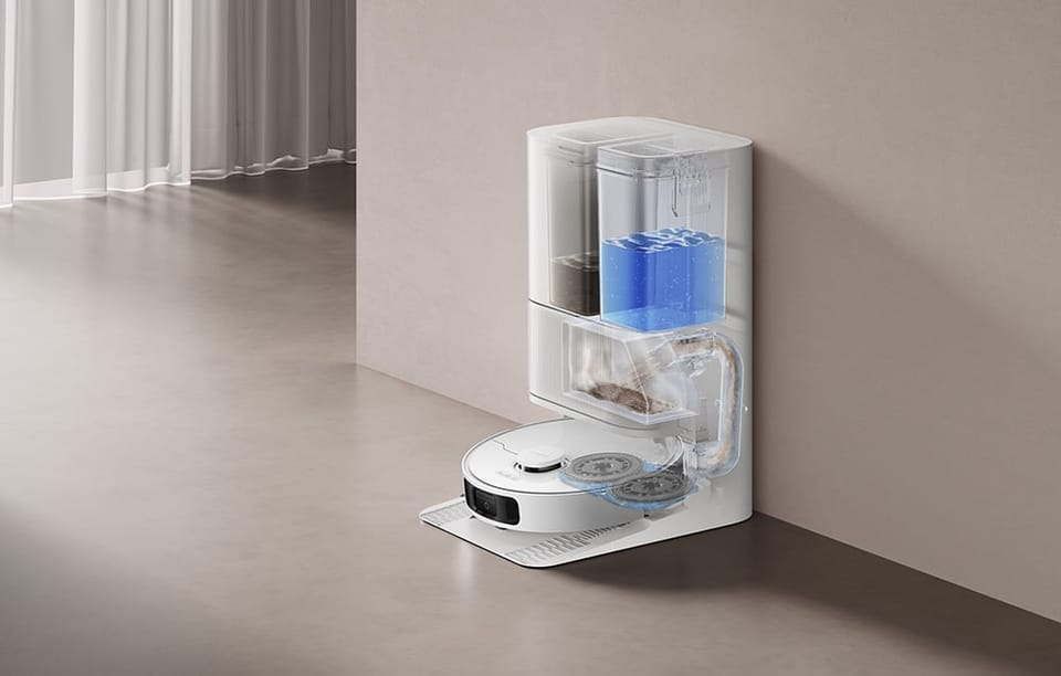 Robot sprzątający w stacji dokującej z widocznymi przezroczystymi zbiornikami na wodę i kurz.