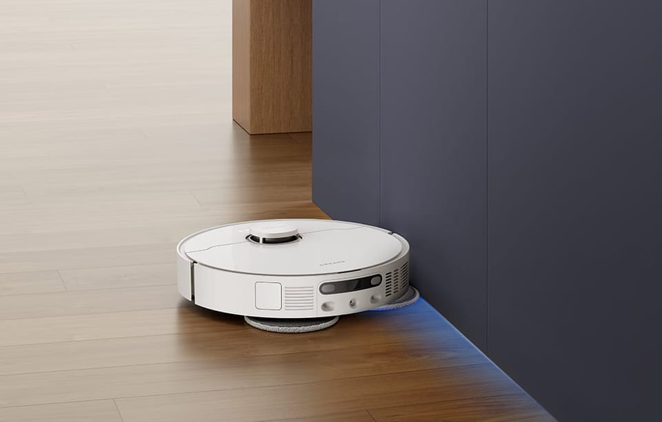 Robot sprzątający czyści podłogę wzdłuż ciemnych szafek na jasnym drewnianym parkiecie.