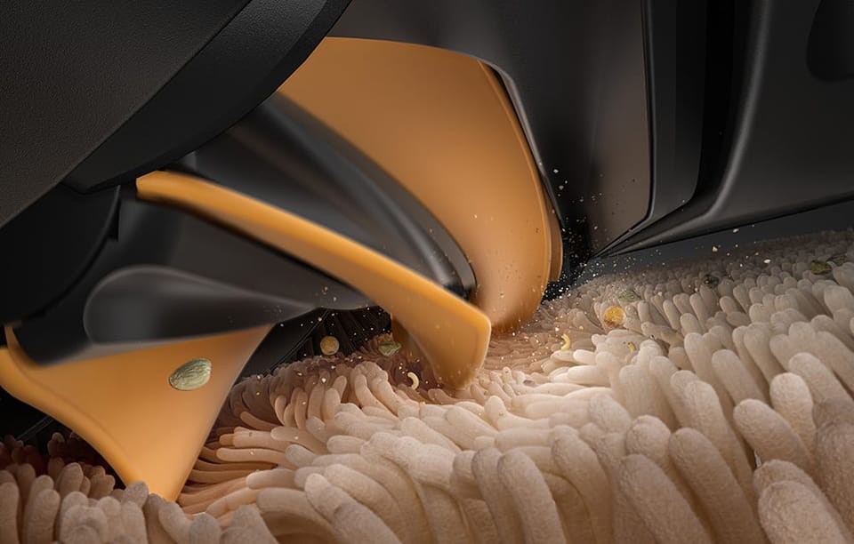 Zbliżenie na szczotkę główną robota sprzątającego podczas pracy na jasnym, puszystym dywanie.