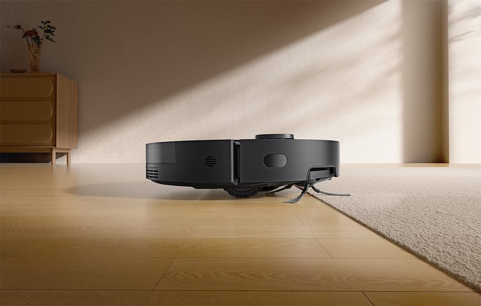 Czarny robot sprzątający Dreame D20 Pro Plus wjeżdża z drewnianej podłogi na jasny dywan.