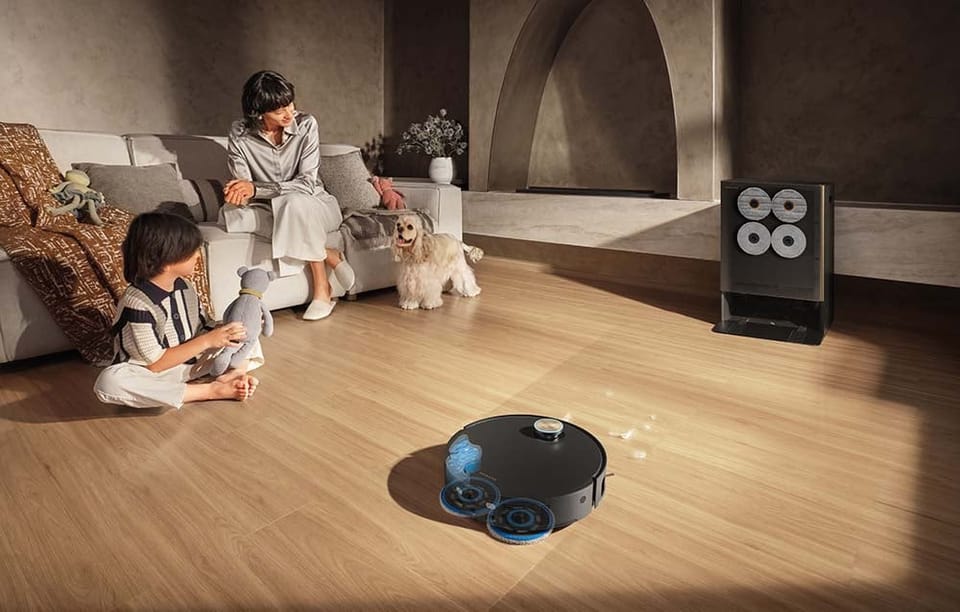 Robot sprzątający Dreame Matrix10 Ultra odkurzający drewnianą podłogę, w tle widać matkę, dziecko i psa.