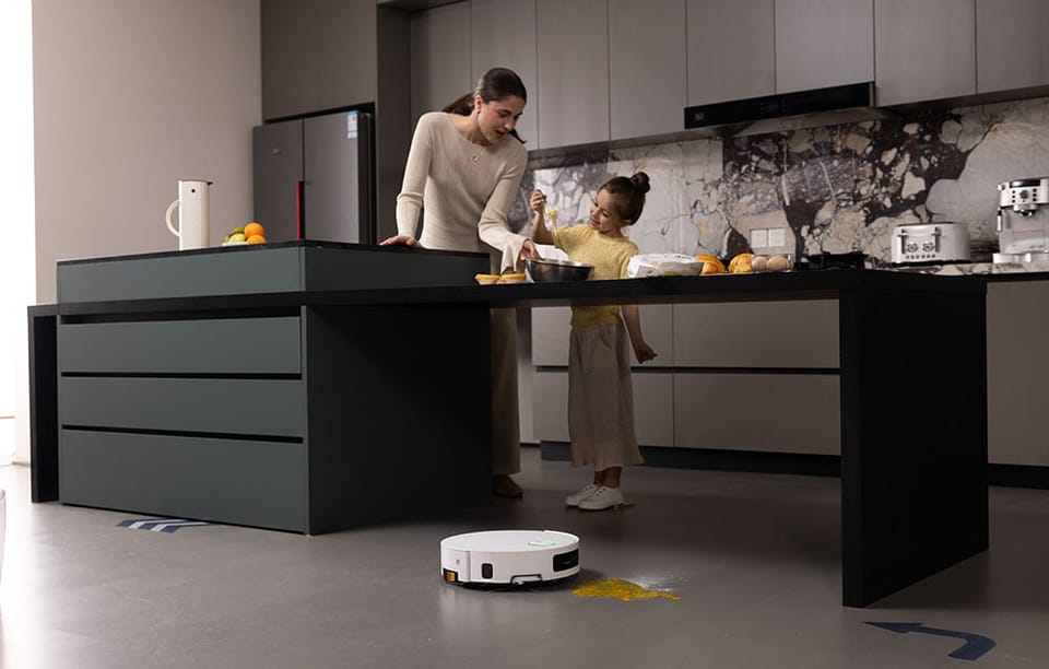 Kobieta i dziewczynka gotują w kuchni, a na podłodze robot sprzątający usuwa rozsypane składniki
