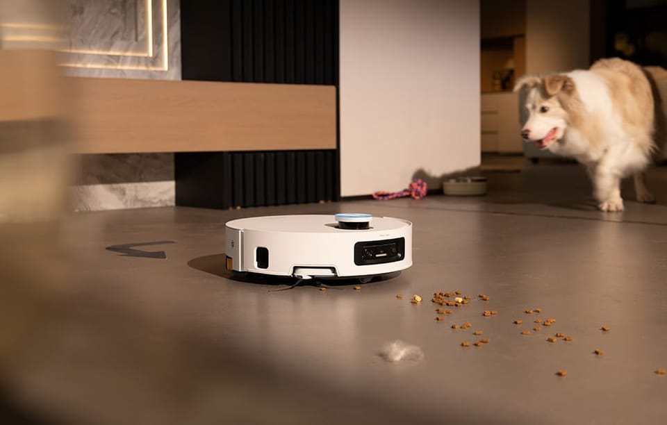 Robot sprzątający zbiera rozsypaną karmę i kłębek sierści z podłogi, obok stoi pies