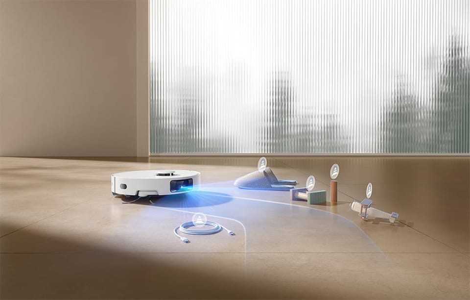 Biały robot sprzątający Dreame D20 Pro z niebieskim światłem z przodu zbliża się do kilku małych przedmiotów leżących na podłodze: kabla USB, szarej skarpetki, zielonej gąbki, rolki papieru i małej zabawki.