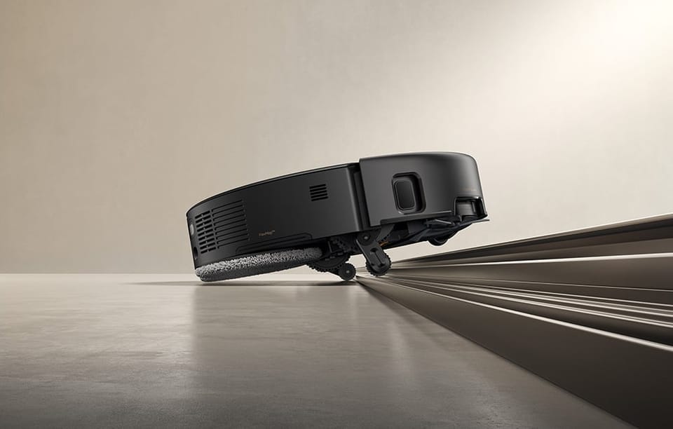 Czarny robot sprzątający pokonuje prowadnicę drzwi.