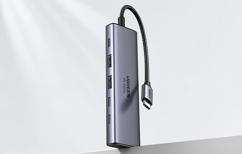Hub UGREEN pokazany pionowo nad krawędzią stołu z widocznym przewodem USB-C i zestawem portów.