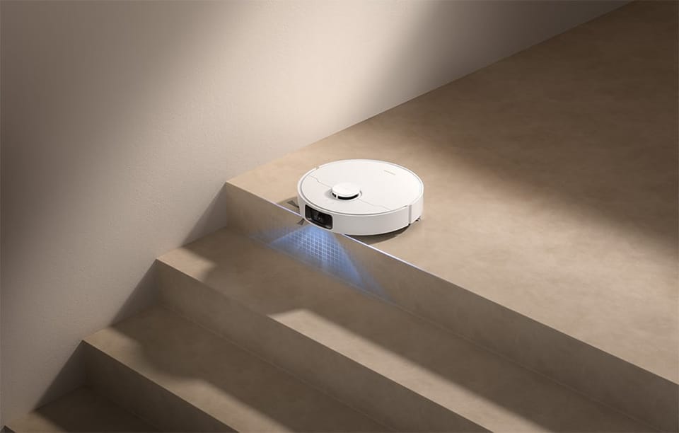 Robot Dreame stoi na krawędzi schodów, skierowany przodem w dół, a spod niego pada niebieskie światło.