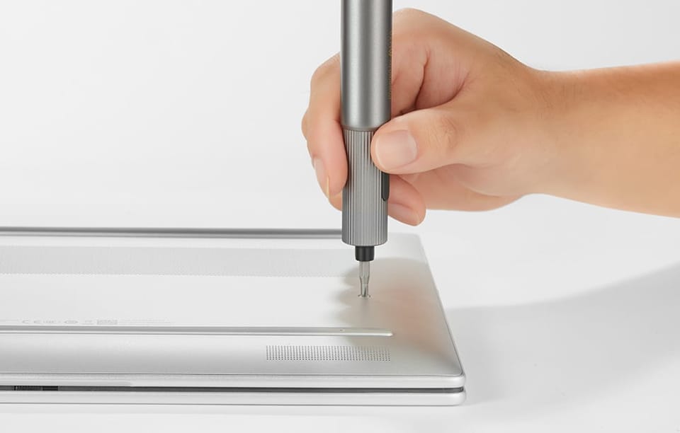 Dłoń wkręcająca śrubę w laptopie wkrętakiem elektrycznym MOVA na szarym tle