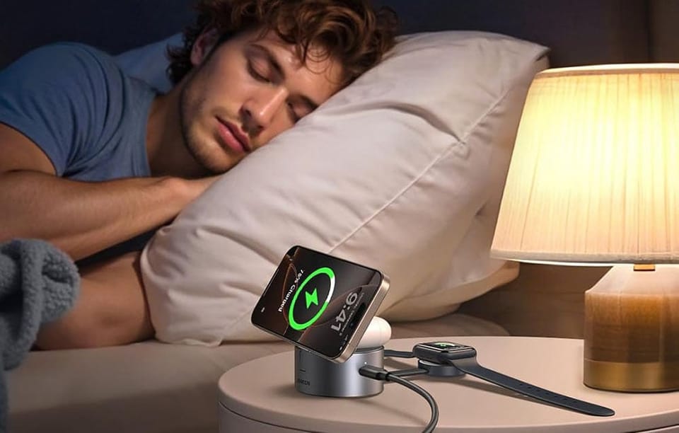 Na szafce nocnej leżą smartfon i smartwatch podłączone do ładowarki bezprzewodowej. Obok śpi mężczyzna.