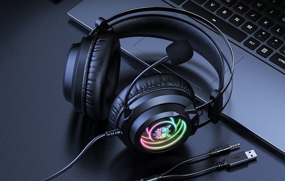 Słuchawki z podświetleniem RGB leżące obok laptopa z kablami USB i jack na ciemnym biurku