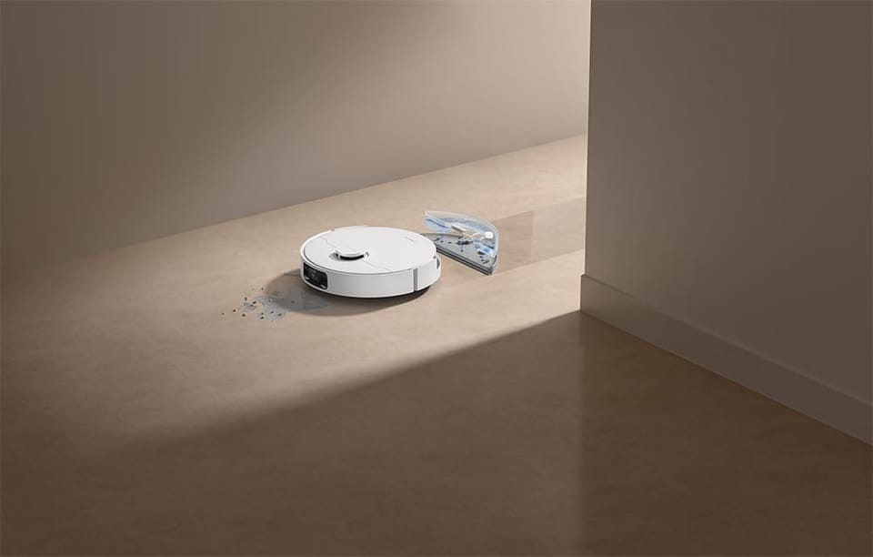 Przed robotem widać rozlaną woda i rozsypane drobinki, a za nim pasek przetartej, wilgotnej podłogi, odbijający delikatnie światło.