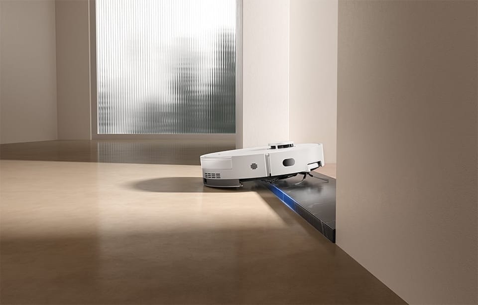 Robot Dreame wjeżdża na próg między pomieszczeniami, podnosząc się na krawędź ciemniejszej powierzchni.