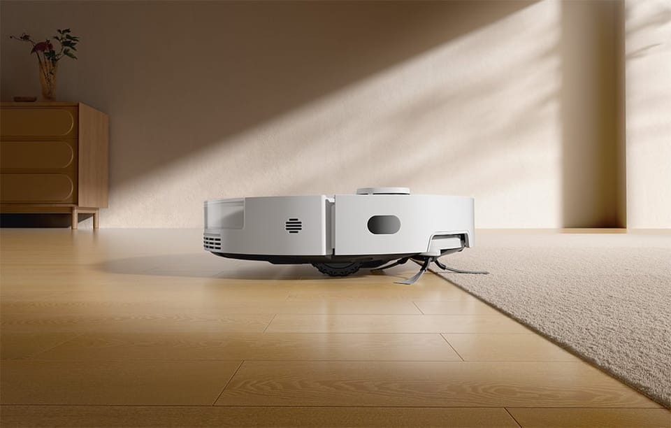 Robot sprzątający Dreame D20 Pro Plus wjeżdża z drewnianej podłogi na jasny dywan w nowoczesnym wnętrzu.