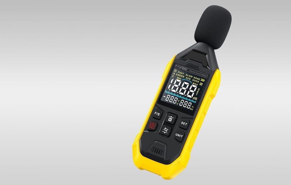 Miernik poziomu dźwięku z osłoną mikrofonu pokazany pod kątem na szarym tle.