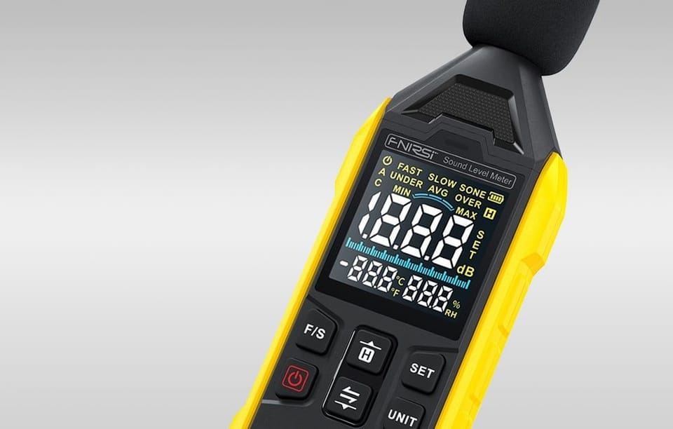 Zbliżenie na wyświetlacz miernika poziomu dźwięku z czytelnymi cyframi i kolorowymi oznaczeniami na szarym tle.