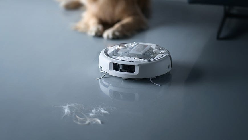 Robot sprzątający zbiera kępki sierści z podłogi, w tle widoczne łapy psa