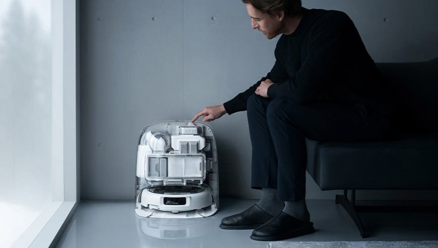 Mężczyzna siedzi na sofie i dotyka górnej części stacji dokującej ROMO z umieszczonym w niej robotem