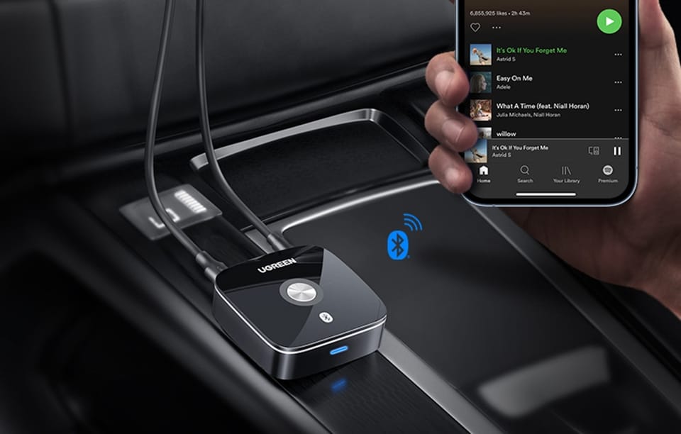 Ręka trzyma smartfon z aplikacją muzyczną obok adaptera Bluetooth w samochodzie