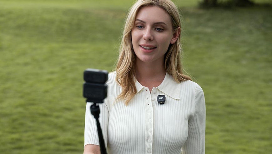 Kobieta nagrywa się kamerą DJI Osmo Nano zamontowaną na statywie, z drugą kamerą przypiętą do kołnierza koszuli