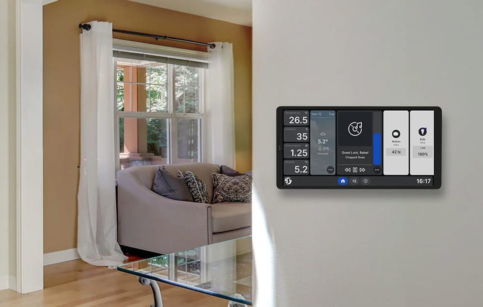 Panel Shelly X2i w srebrnej obudowie na ścianie w salonie, prezentujący kafelki z pogodą, temperaturą i odtwarzaczem muzyki.