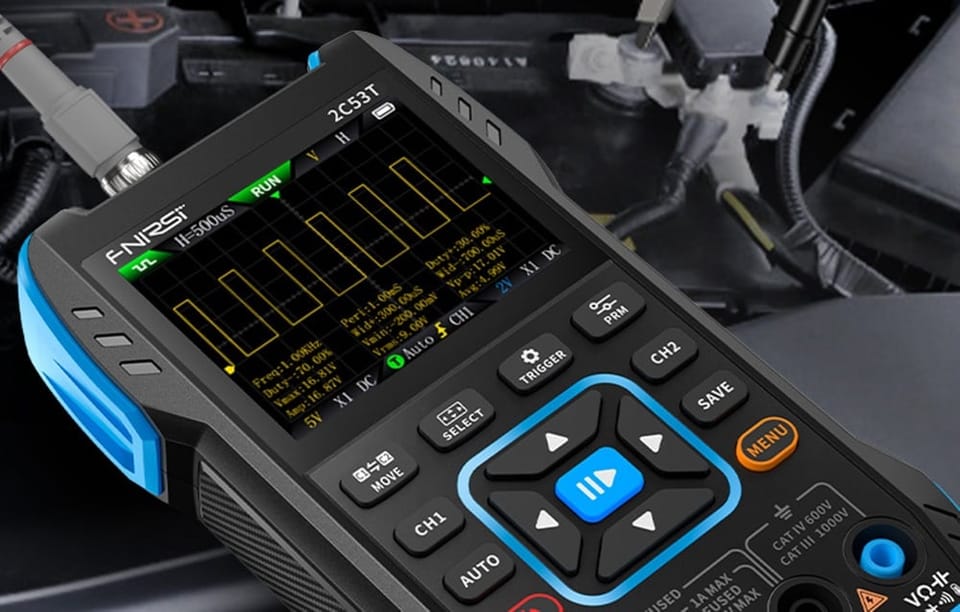 Przyrząd pomiarowy z wykresem fal na ekranie, podłączony przewodem, w tle widoczny przedział silnika.