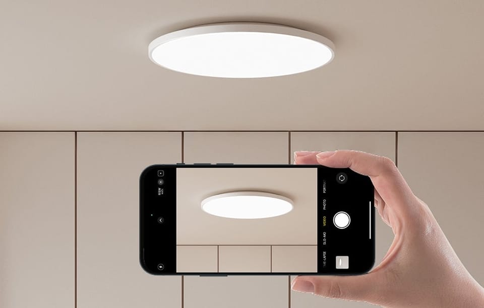 Ręka trzymająca smartfon z aparatem skierowanym na włączoną lampę sufitową Yeelight Mercury C300. 