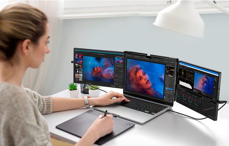 Kobieta przy biurku edytująca zdjęcie portretowe na laptopie z dwoma dodatkowymi ekranami i tabletem graficznym