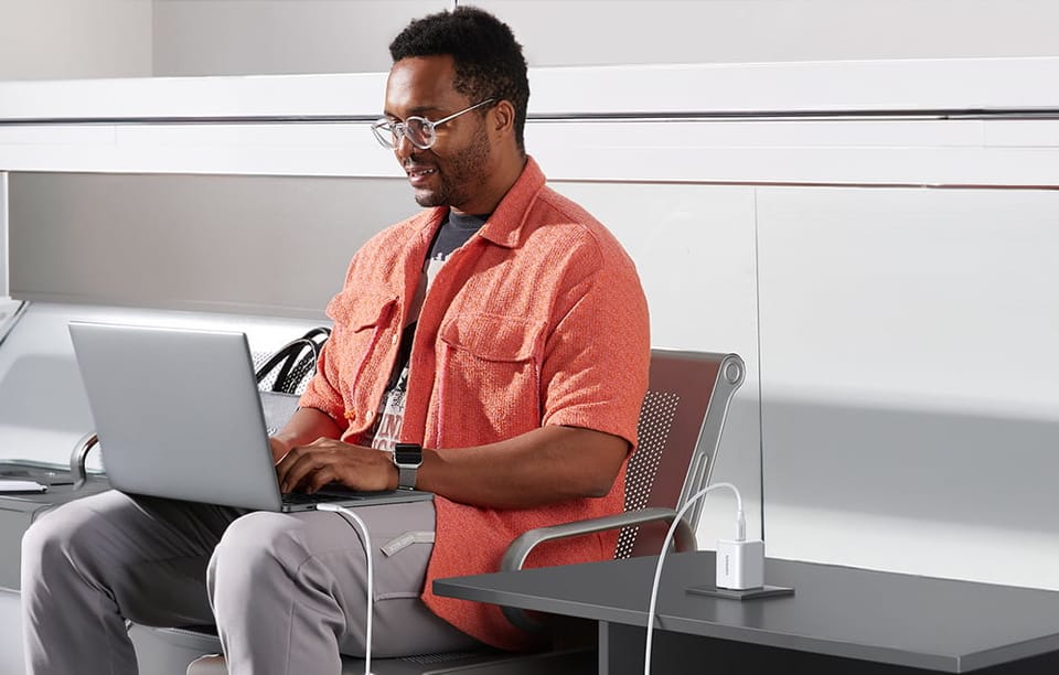 Mężczyzna na lotnisku z laptopem podłączonym kablem do ładowarki 