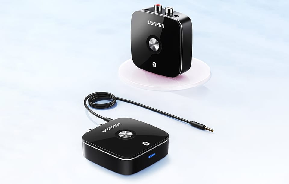 Dwa czarne adaptery Bluetooth UGREEN z kablem audio, jeden na przezroczystej podstawce
