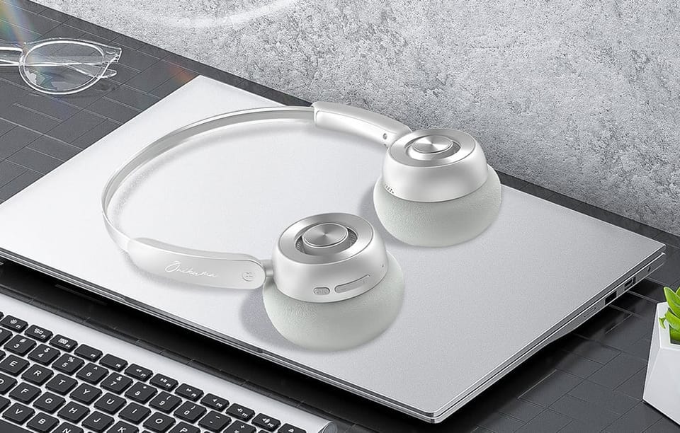 Słuchawki Onikuma leżące na zamkniętym laptopie, obok widać okulary i klawiaturę innego laptopa