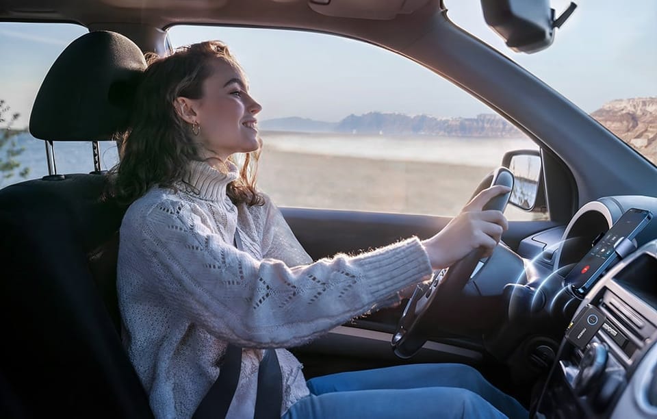 Kobieta w białym swetrze prowadzi samochód na tle górskiego krajobrazu