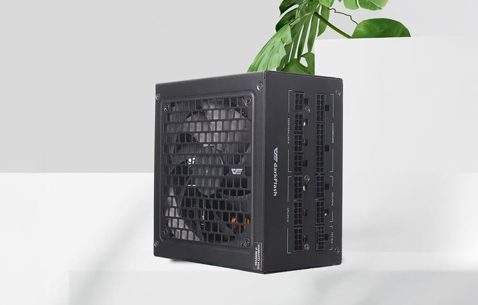 Czarny zasilacz DarkFlash na białym blacie z zieloną rośliną w tle