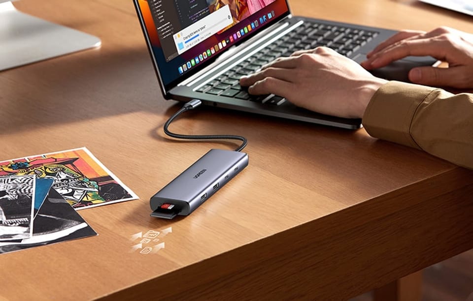 Hub UGREEN z podłączoną kartą SD leżący obok laptopa, przy którym pracuje użytkownik.