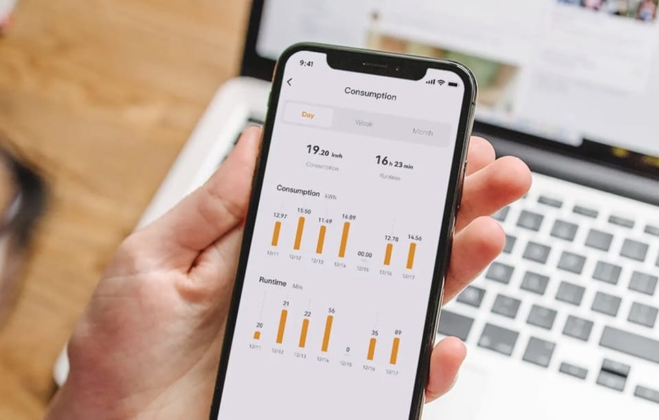 Dłoń trzyma smartfon z aplikacją Consumption pokazującą wykresy zużycia energii elektrycznej i czasu pracy