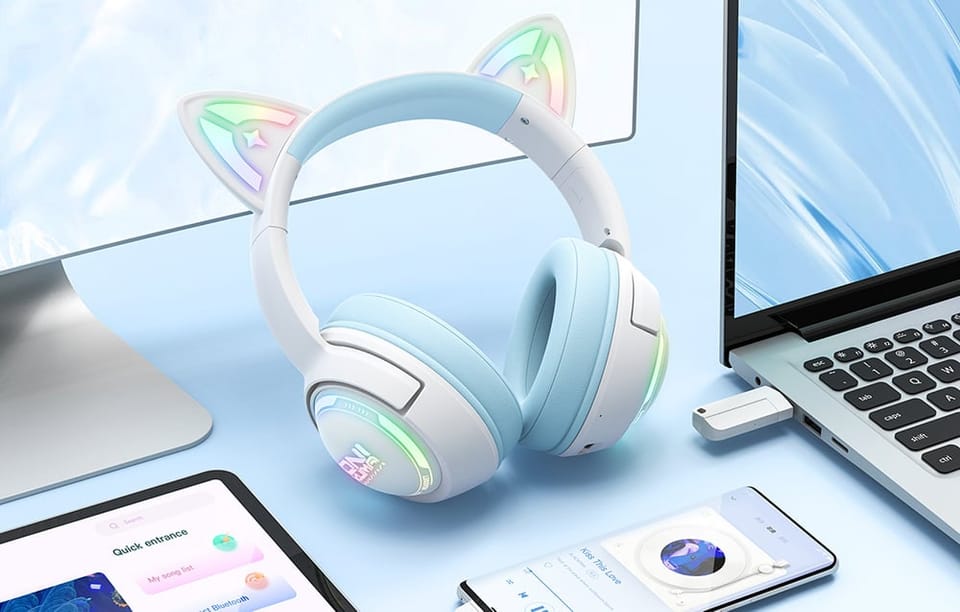 Białe słuchawki z niebieskim akcentem leżące na biurku obok smartfona, tableta, laptopa i monitora