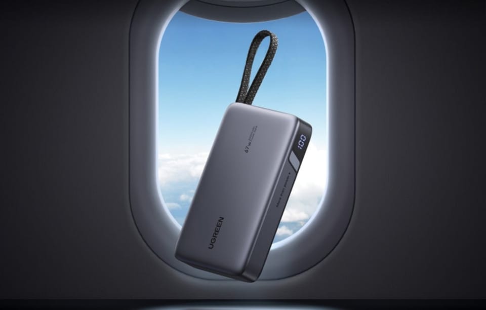 Szary powerbank z wbudowanym kablem na tle okna samolotu
