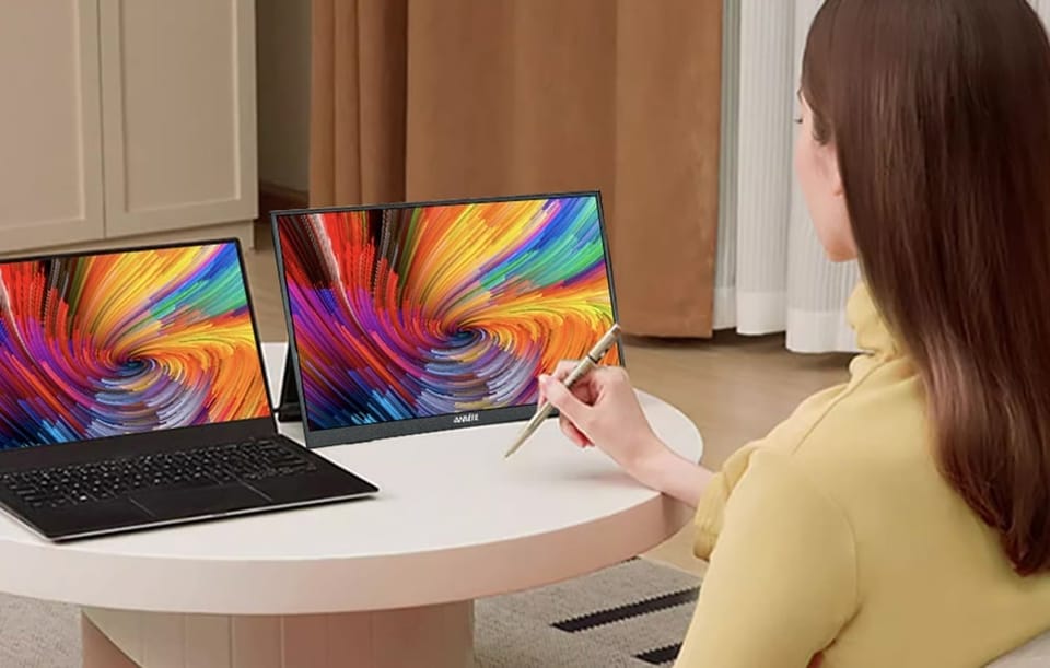 Kobieta rysująca specjalnym rysikiem po dotykowym ekranie monitora stojącego obok laptopa.